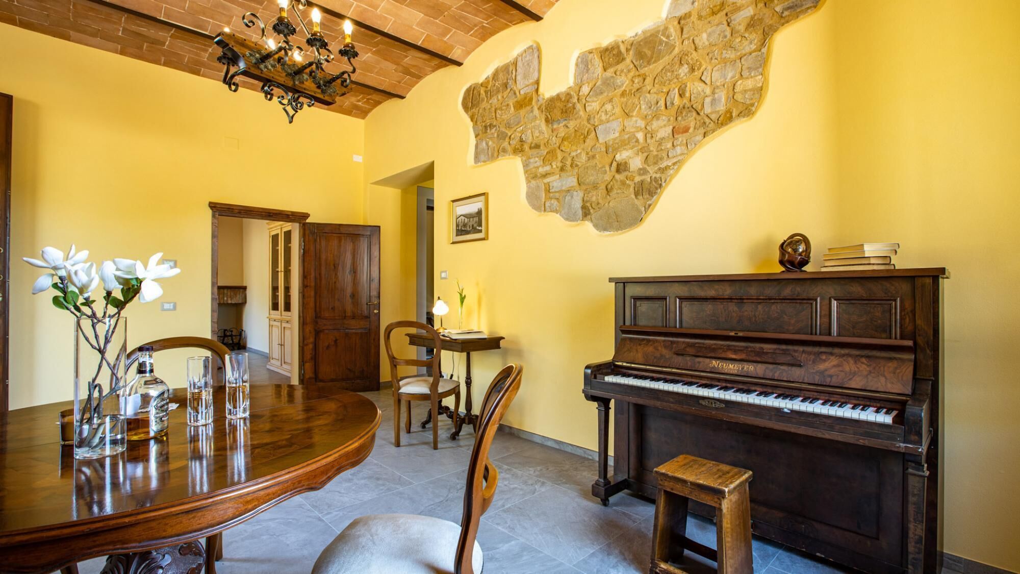 A dining area with a wooden table, chairs, a piano, and a stone wall.