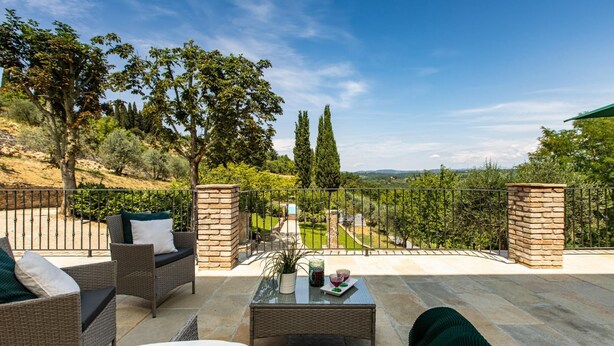 A patio with wicker furniture, a stone table, and a view of a vineyard and hills. - Si-g752-sdto0at - Tenuta di Macericca 10 (Poggibonsi)