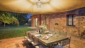 An outdoor patio with a wooden table set for dining, surrounded by stone walls and a brick building.
