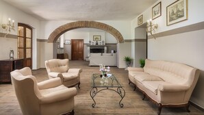 A spacious living room with a high arched brick fireplace, a sofa, two armchairs, and a glass coffee table. - Pg-g601-voan6at - Villa Augusto 10 (Piegaro)