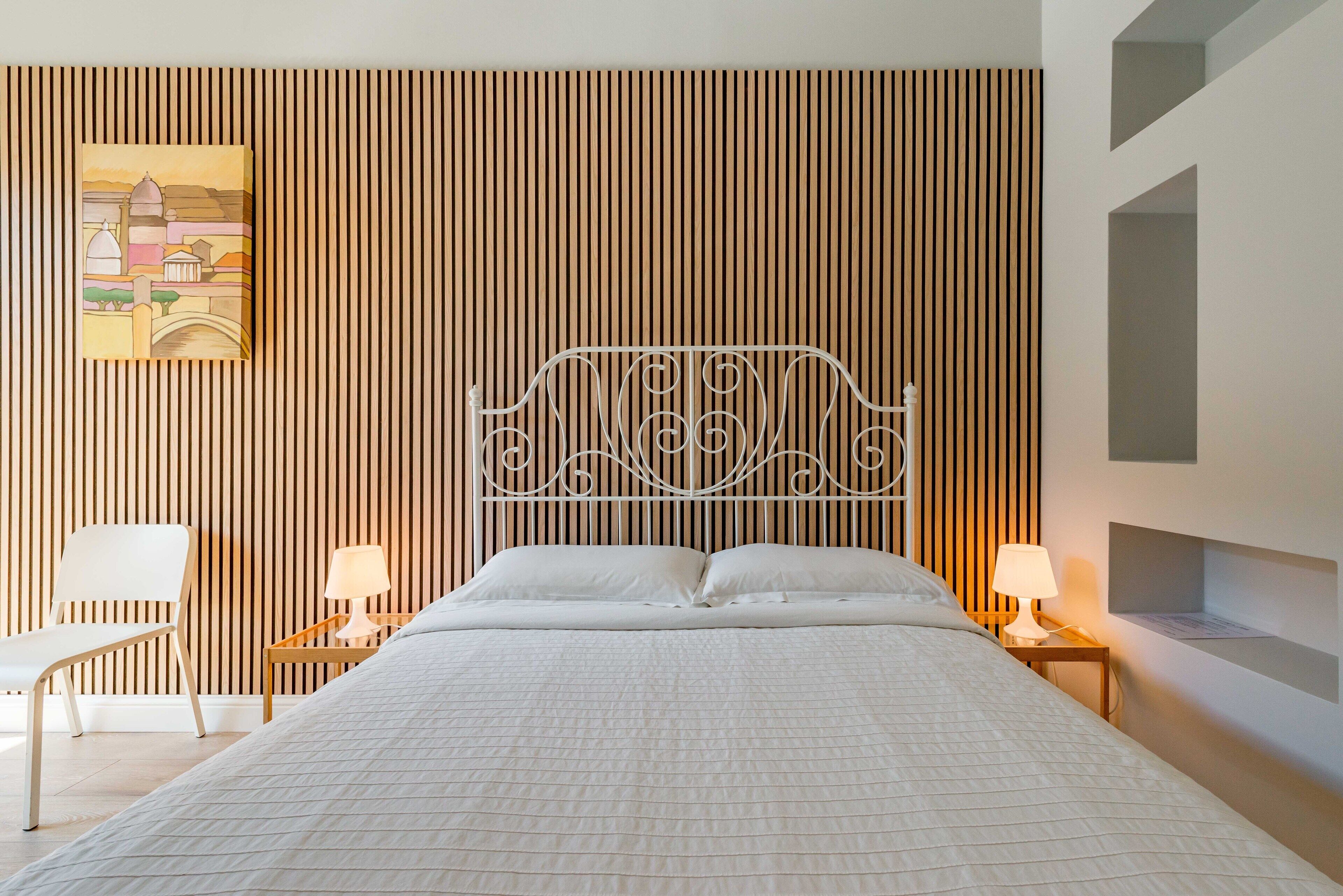 A neatly arranged bedroom with a bed, two bedside tables with lamps, a chair, and a wall-mounted shelf.