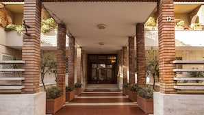 Entrada de hotel con columnas de ladrillo, un corredor cubierto y plantas en macetas.