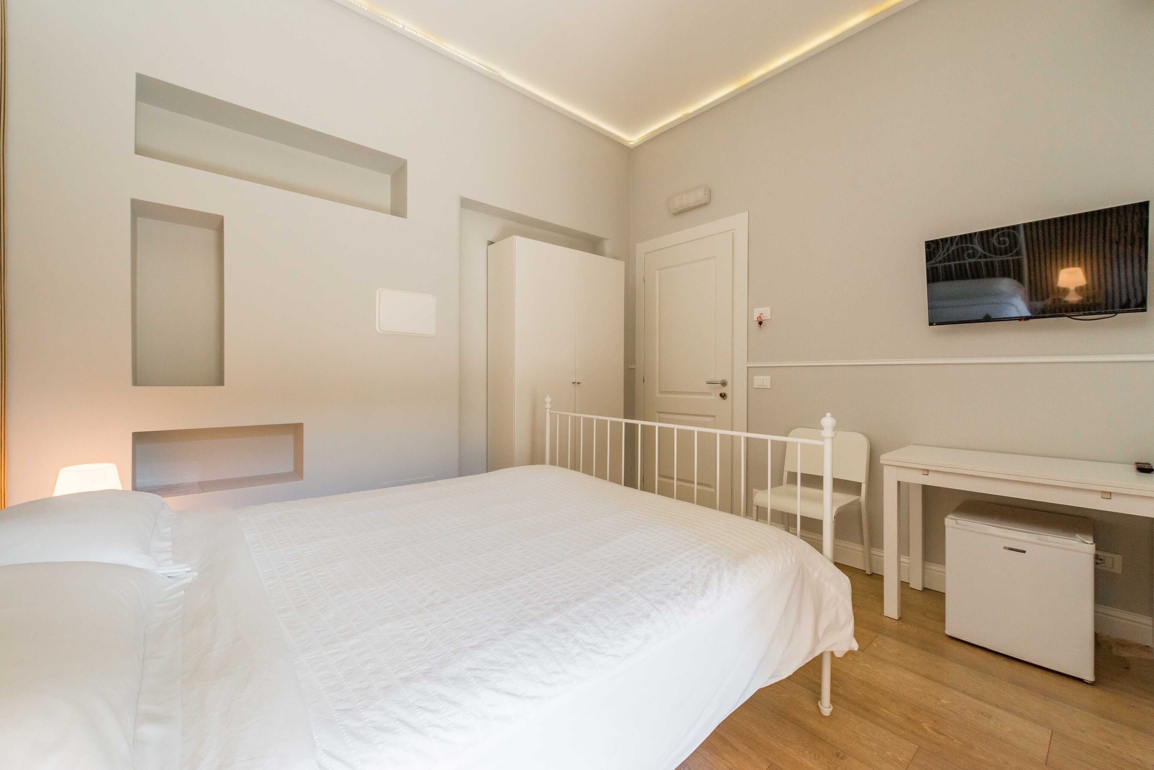 A bedroom with a bed, a desk, and a small refrigerator.