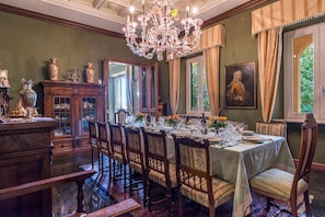 A formal dining room with a long table set for a meal, surrounded by ornate chairs and a chandelier.