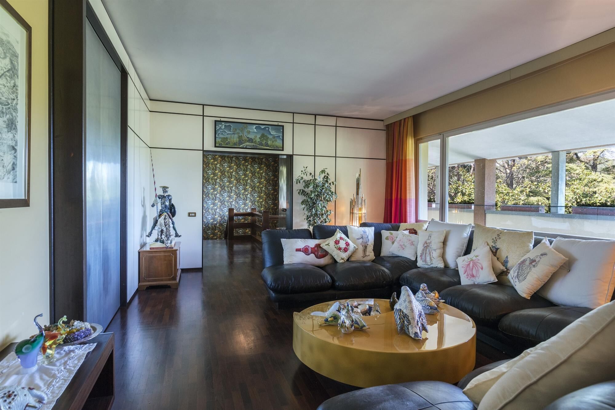 A modern living room with a leather sofa, a round coffee table, and a large window offering a view of greenery outside.