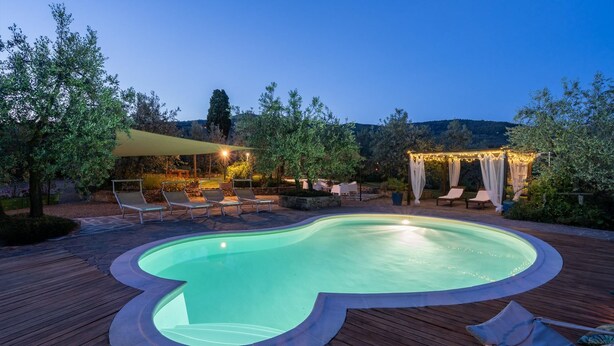 Ein Pool mit Holzterrasse, Liegestühlen und einer Pergola mit Lichterketten.