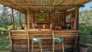Eine rustikale Holztresne mit Bambusdach, zwei Hockern und einer Auswahl an Getränken und Früchten auf der Theke.