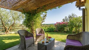 Eine Terrassengruppe mit Korbmöbeln, einem Glastisch und einer Pergola.
