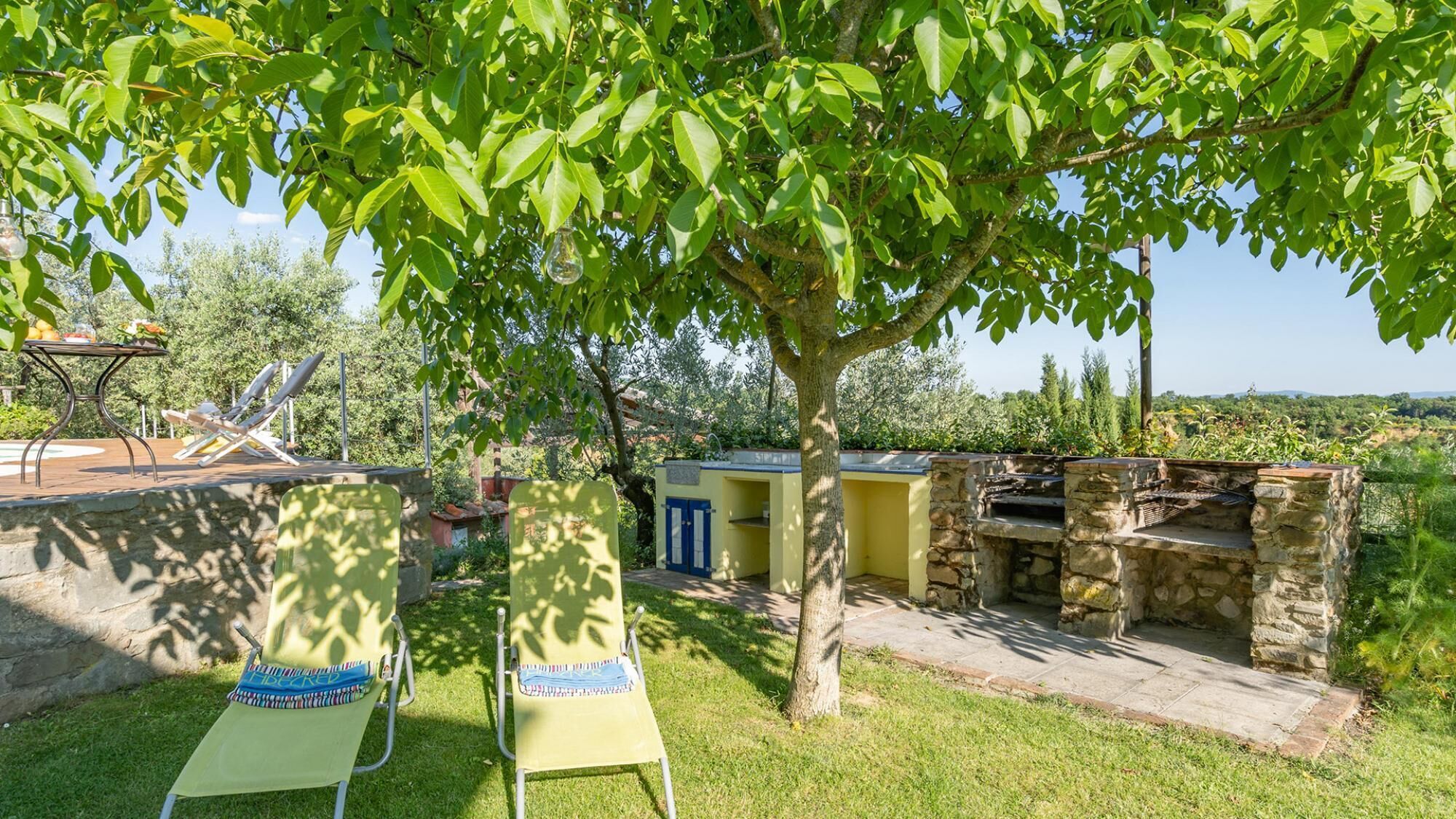 Eine Terrasse mit zwei Liegestühlen, einem Grill aus Stein und einem kleinen Gebäude mit einer blauen Tür.
