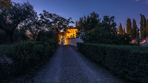 A gravel path leading to a building with a warm light, surrounded by trees and hedges. - Ar-a390-arez0at - Villalta 18 2 (Arezzo)