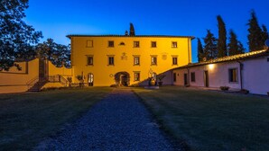 A large yellow building with a central entrance, multiple windows, and a gravel path leading to it. - Ar-a390-arez0at - Villalta 18 2 (Arezzo)