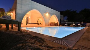 Una piscina con una zona de estar hundida, rodeada por una terraza techada con sillones.