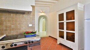 Una cocina con estufa, un bol de verduras y un armario blanco con puertas de vidrio.