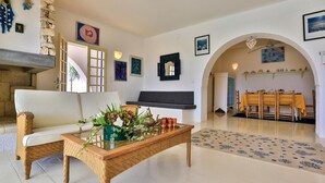 Una sala de estar con un sofá, una mesa de centro con un florero, una chimenea y un comedor con una mesa dispuesta para dos.