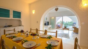 Un comedor con mantel amarillo, platos blancos con diseños azules y vistas a un área de estar exterior a través de un arco.