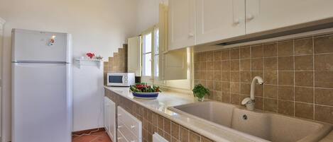 A kitchen with a white refrigerator, a microwave, a sink, and a window with curtains.