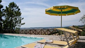 A poolside area with lounge chairs and an umbrella, surrounded by a stone fence and trees, overlooking a landscape with hills. - Pi-m126-pofr0at - Frantusa 6 2 (Volterra)