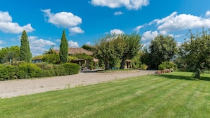 Un jardin bien entretenu, avec un chemin de gravier menant à une maison rustique dotée d’un toit en tuiles.