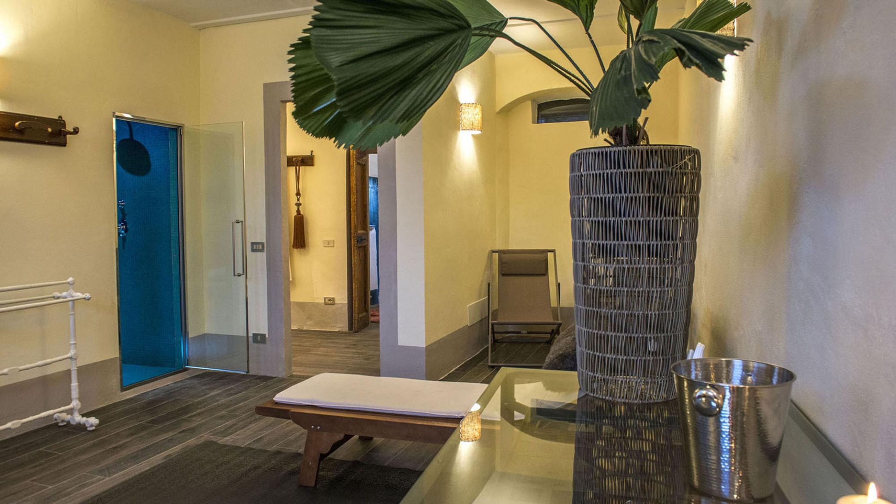 A hallway with a blue door, a bench, a tall decorative vase, and a small table with a candle.
