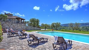 A poolside area with lounge chairs, a stone wall, and a view of the landscape.