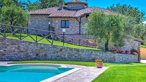 A stone villa with a swimming pool, a stone staircase, and a garden with potted flowers.