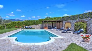 A swimming pool with lounge chairs and a stone wall.