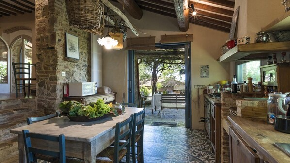 A rustic kitchen with stone walls, a wooden table with chairs, and a view to an outdoor patio.