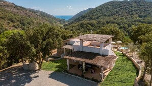 A two-story building with a thatched roof, surrounded by lush greenery and hills. - Villa Zaca 6 in Rio Marina (Rio)