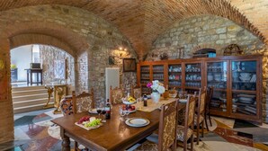 A dining area with a stone vaulted ceiling, a wooden dining table set with plates, glasses, and a fruit platter.