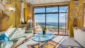 A spacious room with a large window, a sofa, a glass table, and a vase with flowers.