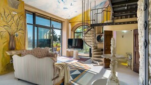 A spacious living room with a large TV, a sofa, and a staircase leading to an upper level.
