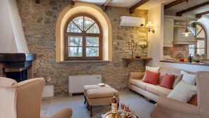 A cozy living room with stone walls, a fireplace, a sofa, and a dining area with a kitchen in the background. - Masso Delle Fanciulle 14 (Pomarance)