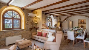 A cozy living room with a stone wall, a large arched window, and a dining area with a long table set for a meal. - Masso Delle Fanciulle 14 (Pomarance)