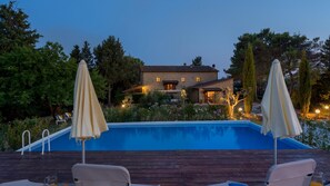 Una piscina con dos sombrillas, una terraza de madera y un edificio de piedra al fondo.