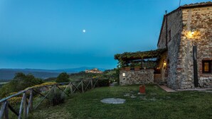 Ein Steinhaus mit Garten, einem Holzzaun und Blick auf ferne Hügel.