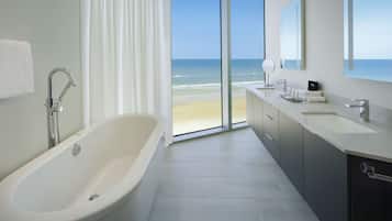 Un baño moderno con bañera, lavamanos y un amplio ventanal con vistas a la playa.