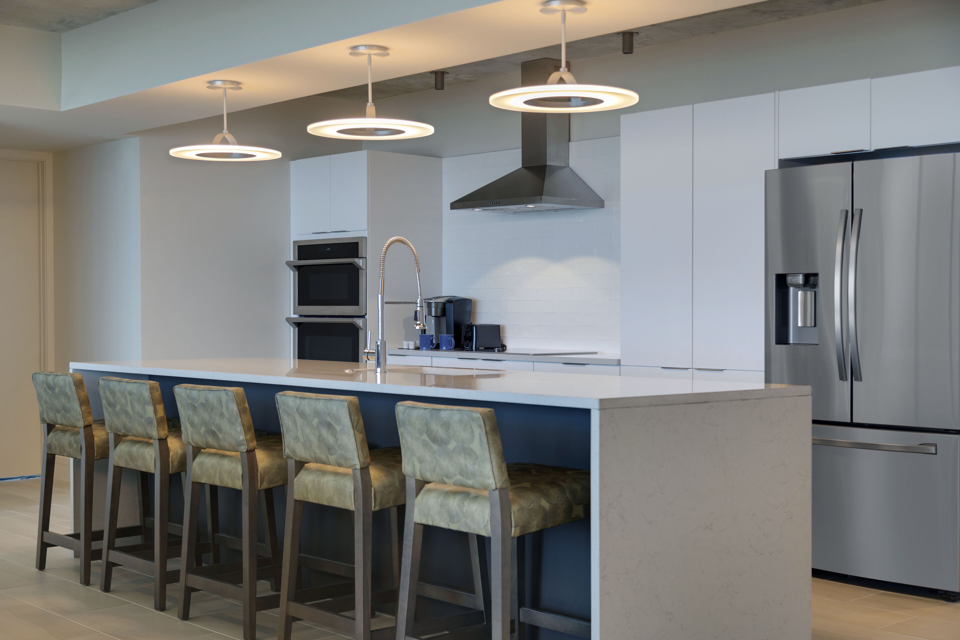A modern kitchen with a central island, bar stools, stainless steel appliances, and pendant lighting.