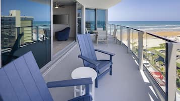 A balcony with a view of the beach, furnished with blue chairs and a small table.