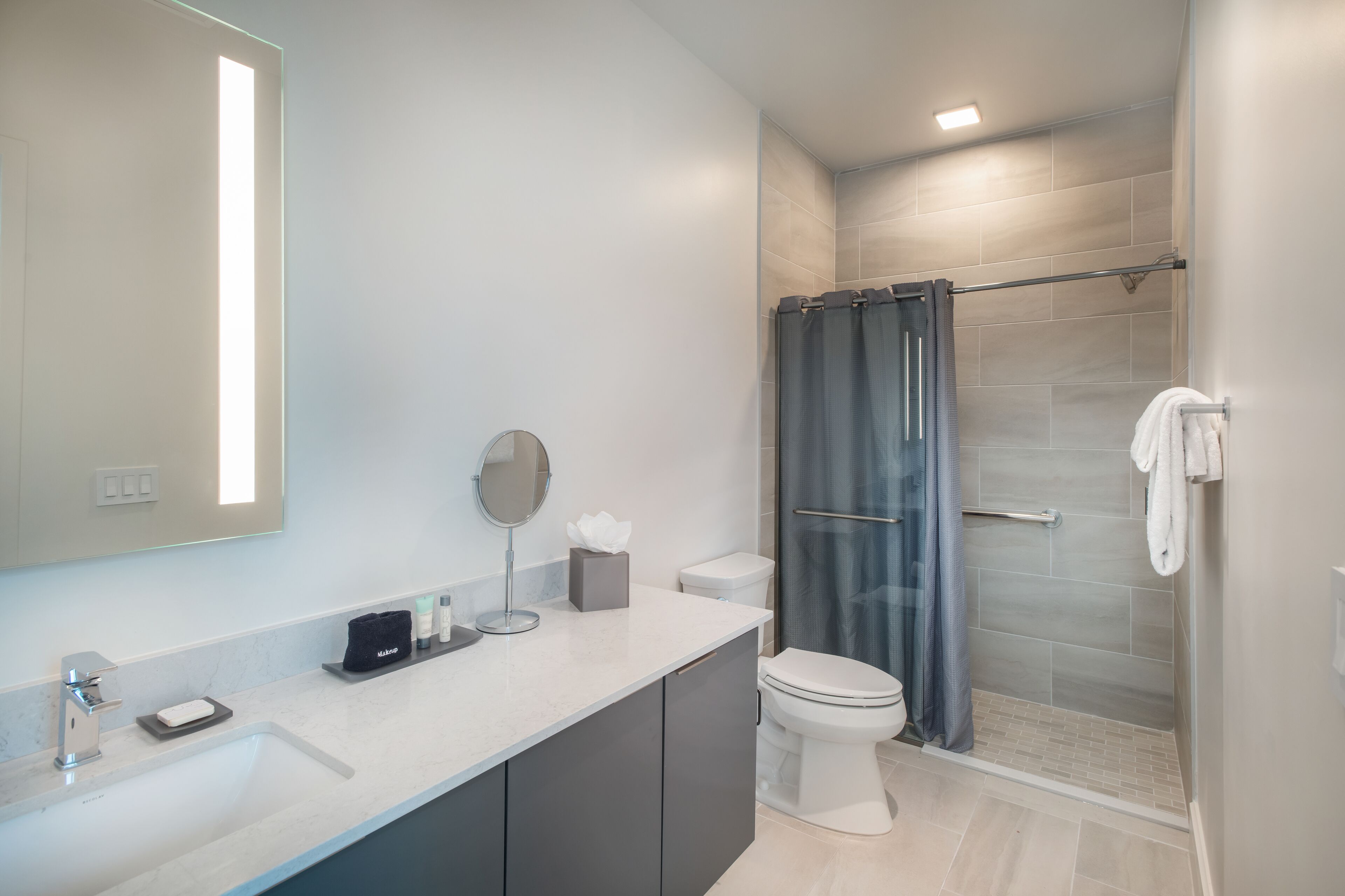 Un baño moderno con un espejo grande, un lavamanos, un inodoro y una zona de ducha.