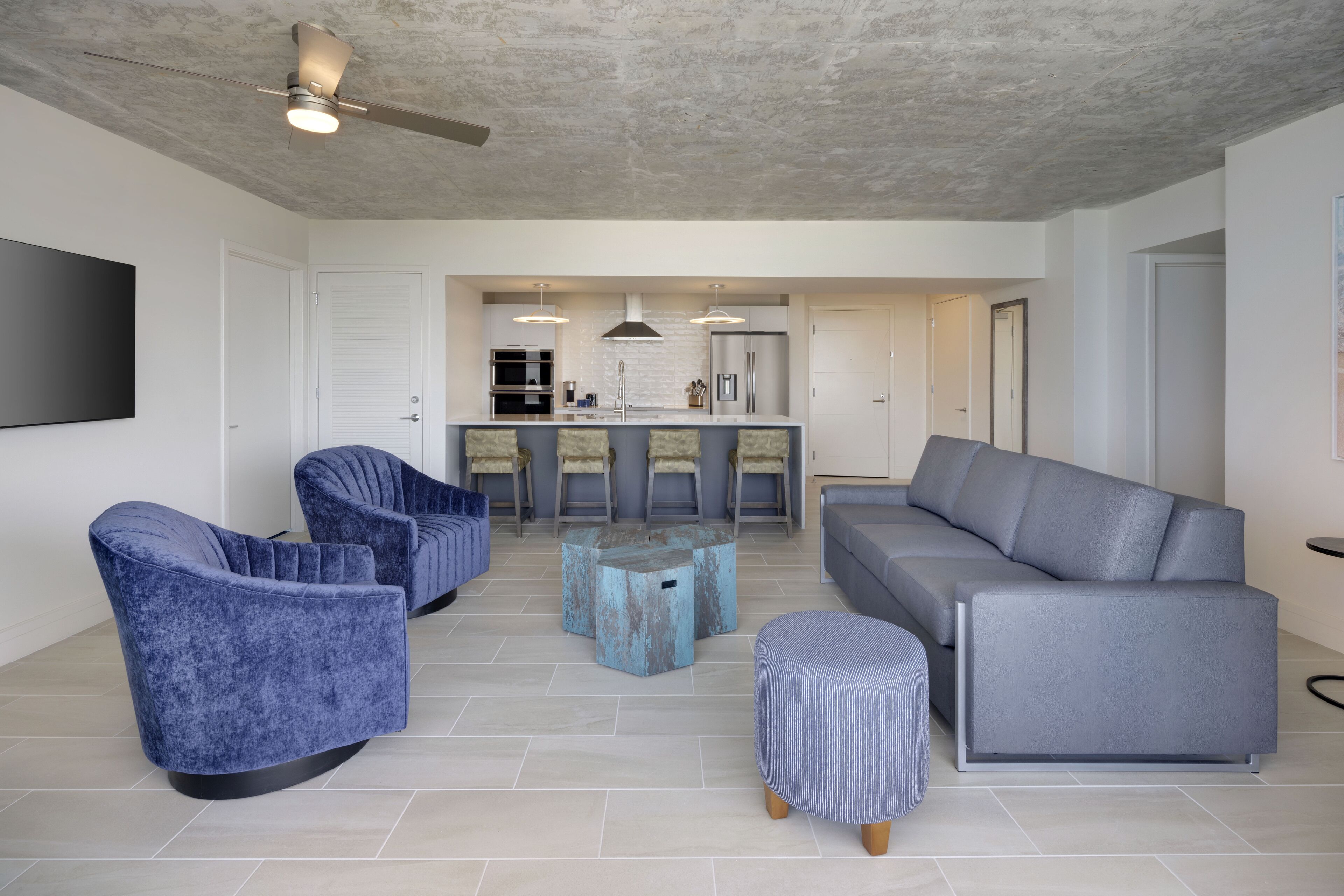 Una sala moderna con un sofá gris, sillones azules y una mesa de centro.