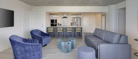 Una sala moderna con un sofá gris, sillones azules y una mesa de centro.