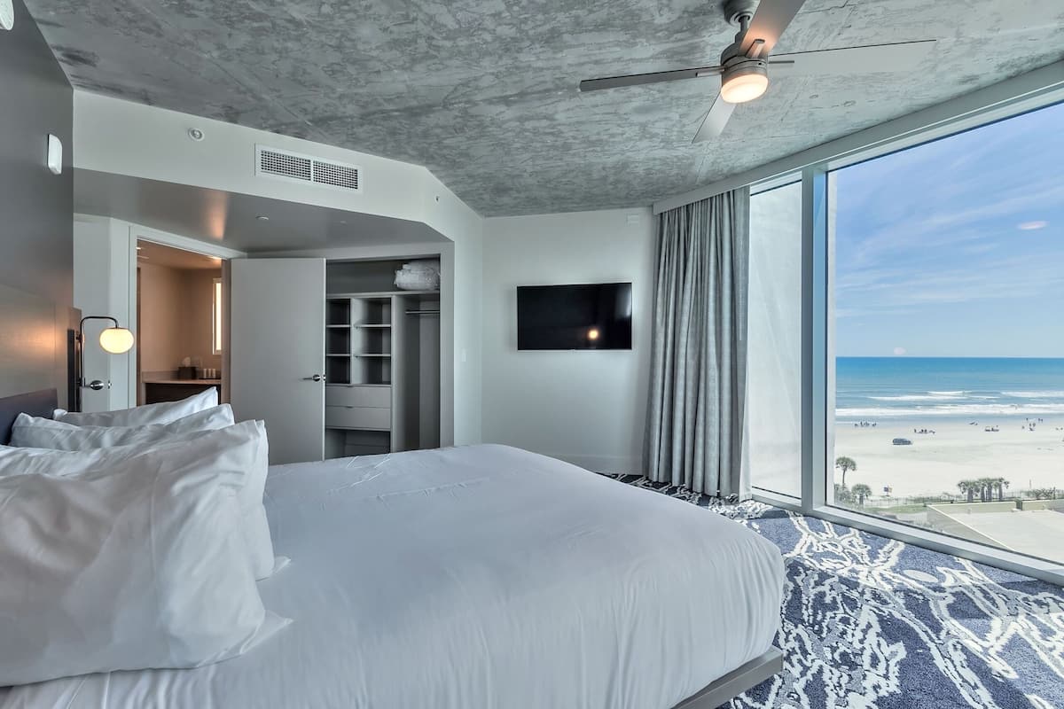 A modern hotel room with a large bed, a flat-screen TV, and a view of the beach.