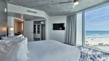 Une chambre d’hôtel moderne dotée d’un grand lit, d’une télévision à écran plat et offrant une vue sur la plage.