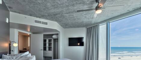 A modern hotel room with a large bed, a flat-screen TV, and a view of the beach.
