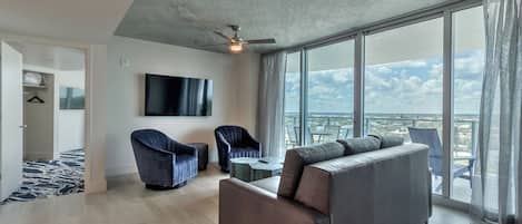 A modern living room with a large sofa, two armchairs, a TV, and a balcony with a city view.
