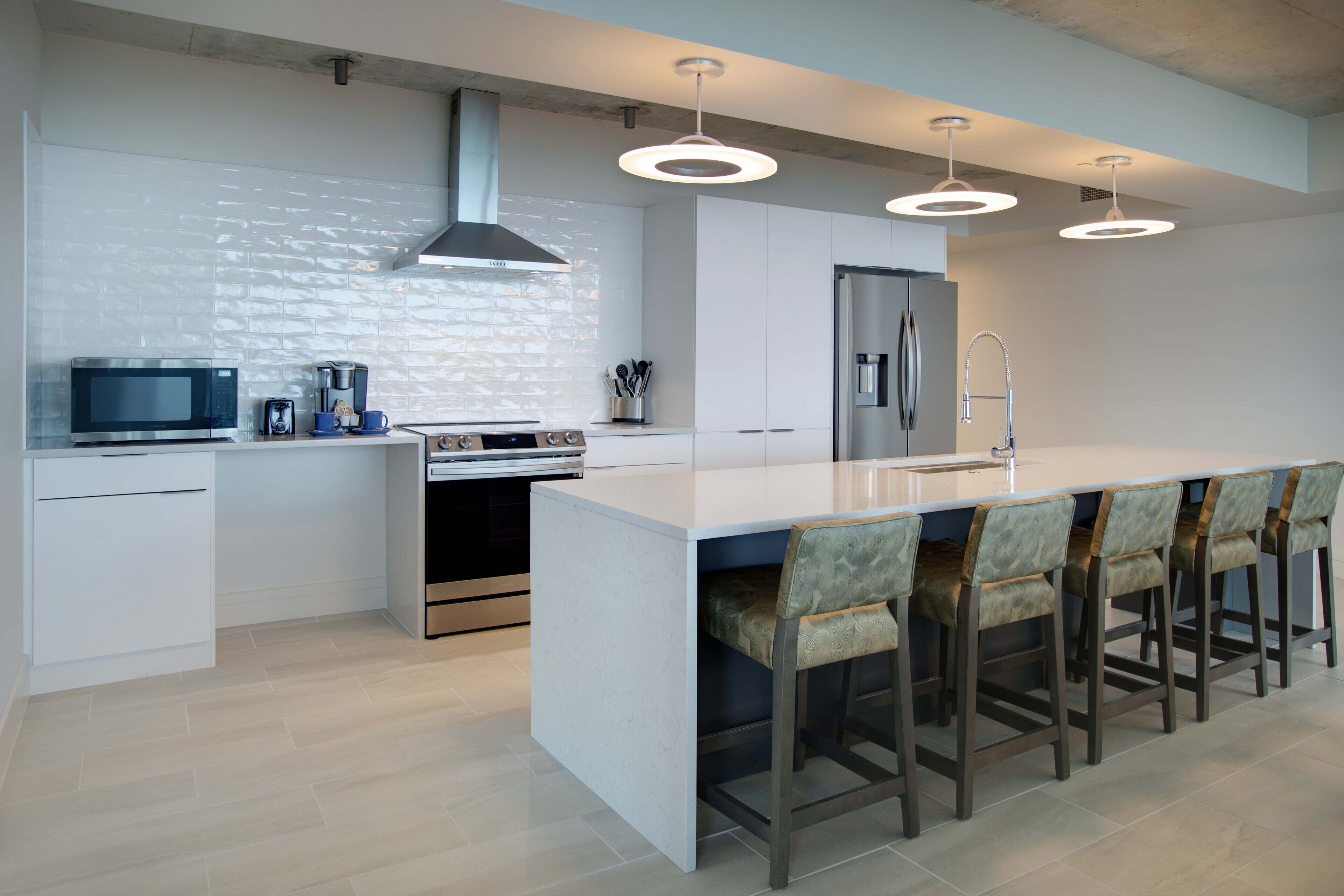 A modern kitchen with a large island, bar stools, a microwave, a coffee maker, and a stainless steel refrigerator.