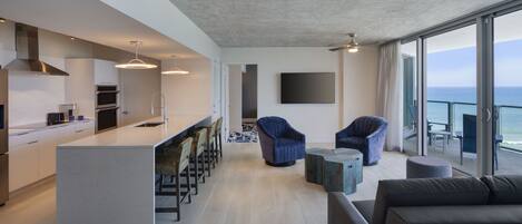 A modern kitchen with a central island, bar seating, and a large window overlooking the sea.