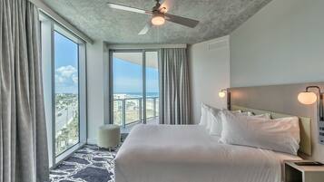 A hotel room with a large bed, a ceiling fan, a view of the city, and a balcony.