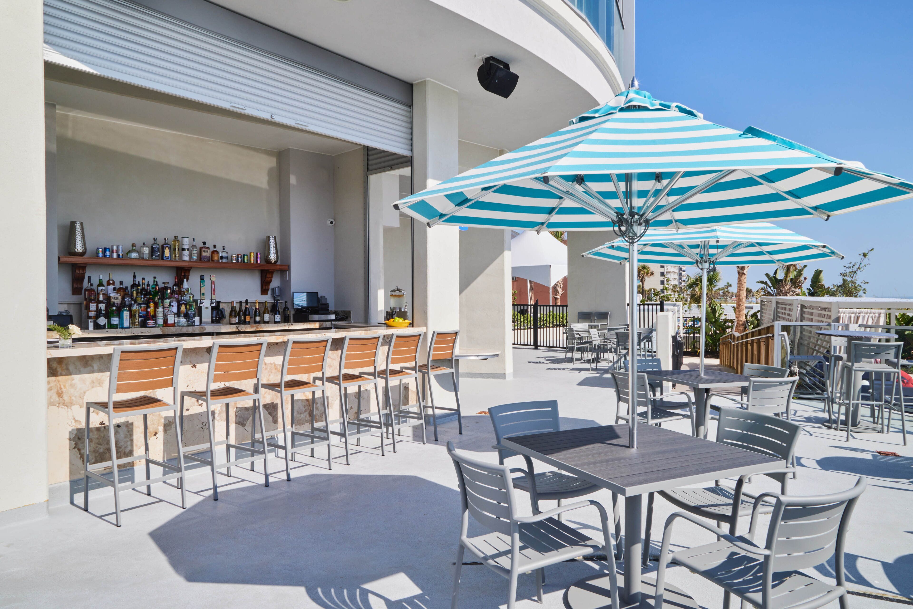 An outdoor bar area with a counter, bar stools, and striped umbrellas.