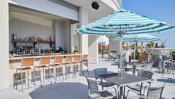 An outdoor bar area with a counter, bar stools, and striped umbrellas.